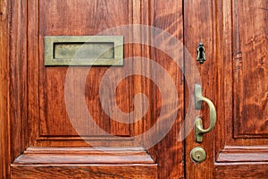 Fragment of wood front door with brass mailbox, door handle, key hole and the lock