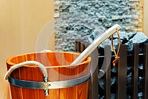 A fragment of a wooden bucket in the bath. Equipment for a sauna on a background of a fireplace with stones