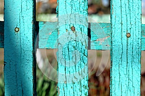 Fragment of a wooden rural fence made from painted green aged planks on the background of garden plants in bokeh