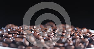 Fragrant coffee beans spin in a white plate to the right and left on a black background