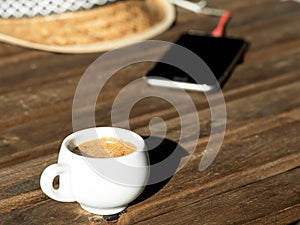 Fragrant espresso coffee on a wooden table. In the background is a straw hat and a telephone. Close-up