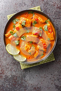 Fragrant fish curry of white fish fillet with coconut, tomatoes and Asian spices close-up on a plate on the table. Vertical top