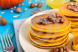 Fragrant golden pumpkin pancakes with honey and walnuts on a blue wooden background.