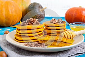 Fragrant golden pumpkin pancakes with honey and walnuts on a blue wooden background.