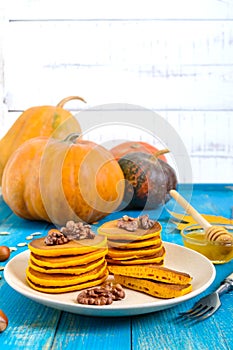 Fragrant golden pumpkin pancakes with honey and walnuts on a blue wooden background.