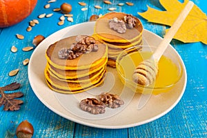 Fragrant golden pumpkin pancakes with honey and walnuts on a blue wooden background