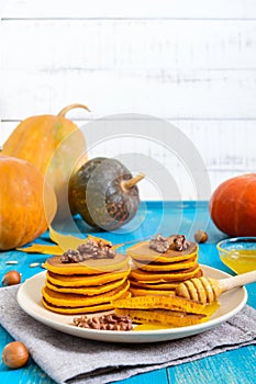 Fragrant golden pumpkin pancakes with honey and walnuts on a blue wooden background