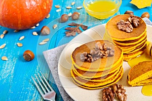 Fragrant golden pumpkin pancakes with honey and walnuts on a blue wooden background.