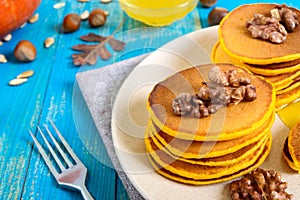 Fragrant golden pumpkin pancakes with honey and walnuts on a blue wooden background.