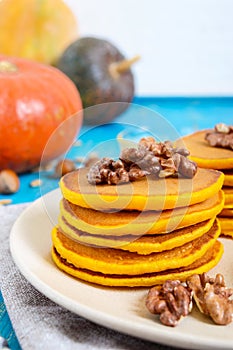 Fragrant golden pumpkin pancakes with honey and walnuts on a blue wooden background.