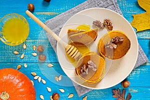 Fragrant golden pumpkin pancakes with honey and walnuts on a blue wooden background.