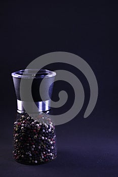 Fragrant multicolor peppercorns in a pepper shaker on a black background