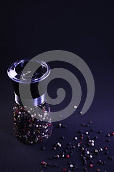 Fragrant multicolor peppercorns in a pepper shaker on a black background