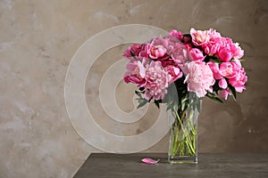 Fragrant peonies in vase on table against color background. Beautiful spring flowers