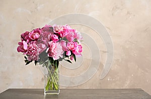 Fragrant peonies in vase on table against color background. Beautiful spring flowers