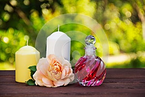 Fragrant rose oil in a beautiful glass bottle. Pink elixir, candles and flowers. Spa concept. Romantic concept.