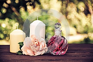 Fragrant rose oil in a beautiful glass bottle. Pink elixir, candles and flowers. Spa concept. Vintage tinting