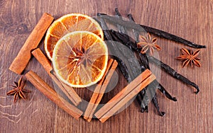 Fragrant vanilla, cinnamon, star anise and dried orange on wooden surface