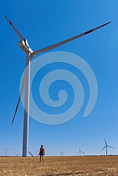 A frail Girl stands in a mown field next to the wind turbines