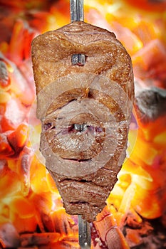 Fraldinha, bovine kind of flank steak, traditional brazilian barbecue whole piece on skewer isolated on blurred ember background