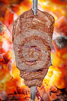 Fraldinha, bovine kind of flank steak, traditional brazilian barbecue whole piece on skewer isolated on blurred ember background