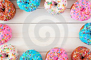 Frame of assorted donuts with pastel icing against white wood