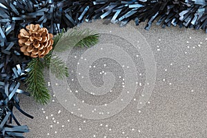 Frame with blue tinsel, a pine cone and fresh pine brunches, and sparkling confetti stars spread against a silver gray background