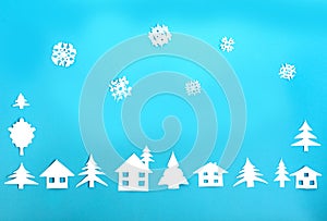 Frame made of white paper figures - houses, Christmas trees, snowflakes on a blue background