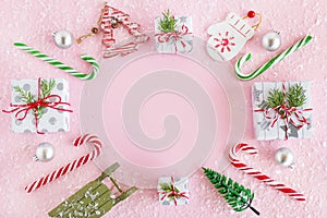 Frame from colorful Christmas decorations, caramel sticks and gift boxes with artificial snow on a pink background.