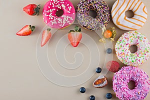 Frame of colorful doughnuts with different kinds of topping and fruits on light background.