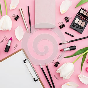Frame composition with clipboard, tulips, cosmetics and accessory on pink background. Top view. Flat lay. Home feminine desk.