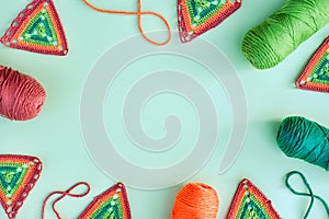 Frame of crochet motifs, skeins of yarn and crochet cords on light green background.