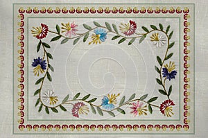 Frame with embroidered satin stitch patterns of branchlets with leaves, and red, blue, purple,cornflowers on the cotton fabric photo