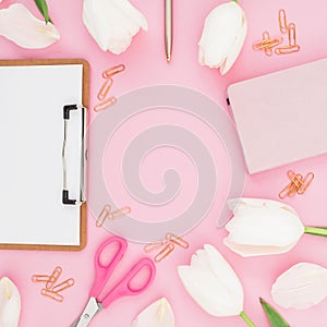 Frame with flowers, clipboard, clips, notebook and scissors on pink background. Flat lay, top view