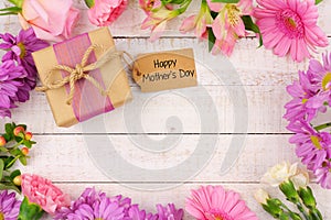 Frame of flowers with Mothers Day gift and tag against white wood