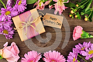 Frame of flowers with Mothers Day gift and tag against rustic wood