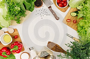 Frame of fresh green salad, red paprika, cherry tomato, pepper, oil and kitchenware on soft white wooden board.