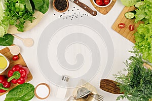 Frame of fresh green salad, red paprika, cherry tomato, pepper, oil and kitchenware on soft white wooden board. Healthy eating bac