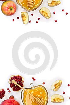 Frame of honey in glass bowl, red apples, garnets, wooden dipper on a white background with space for text. Top view, flat lay