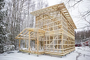 frame house construction in winter, under the snow, in the forest. Fresh wood, frame of a two-story house