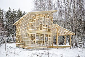 frame house construction in winter, under the snow, in the forest. Fresh wood, frame of a two-story house