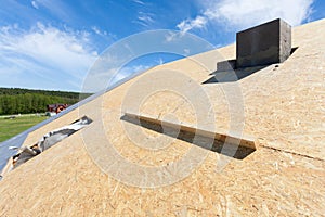 Frame house under construction. Roof with installed fiber board and plastic mansard or skylight window.