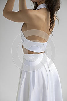 Frame image of a young brunette woman with hairstyle and makeup in sensual white dress posing in studio.