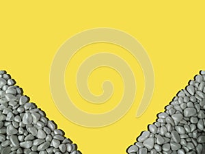 Frame in lower corners ultimate gray sea pebbles with shadow,illuminating yellow on background.Summer vacation concept.Rectangular