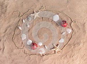 Frame made of christmas balls, beads, starfishes and seashells on sand beach. Christmas and New Year celebration
