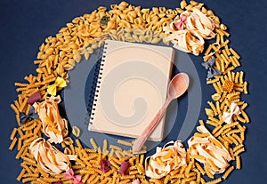 Frame made of different kinds of raw pasta and empty note book for your text