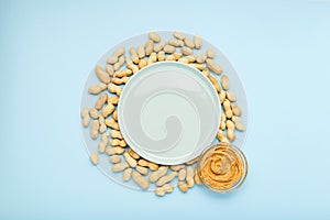 Frame made of nuts peanuts in shell with copy space in center on blue colored background with creamy peanut paste in open glass
