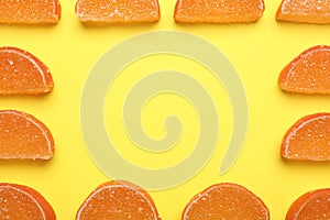 Frame made with orange marmalade candies on yellow background, flat lay. Space for text