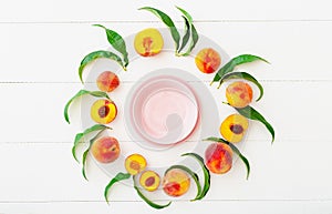 Frame made of peaches and peach tree leaves with pink empty plate in center. Flat lay with copy space. Whole peaches and half