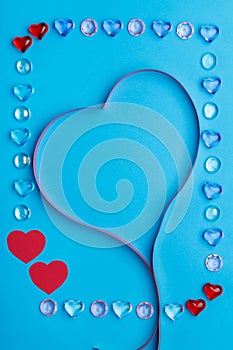 In a frame made of pebbles of hearts on a blue background, a ribbon in the shape of a heart.